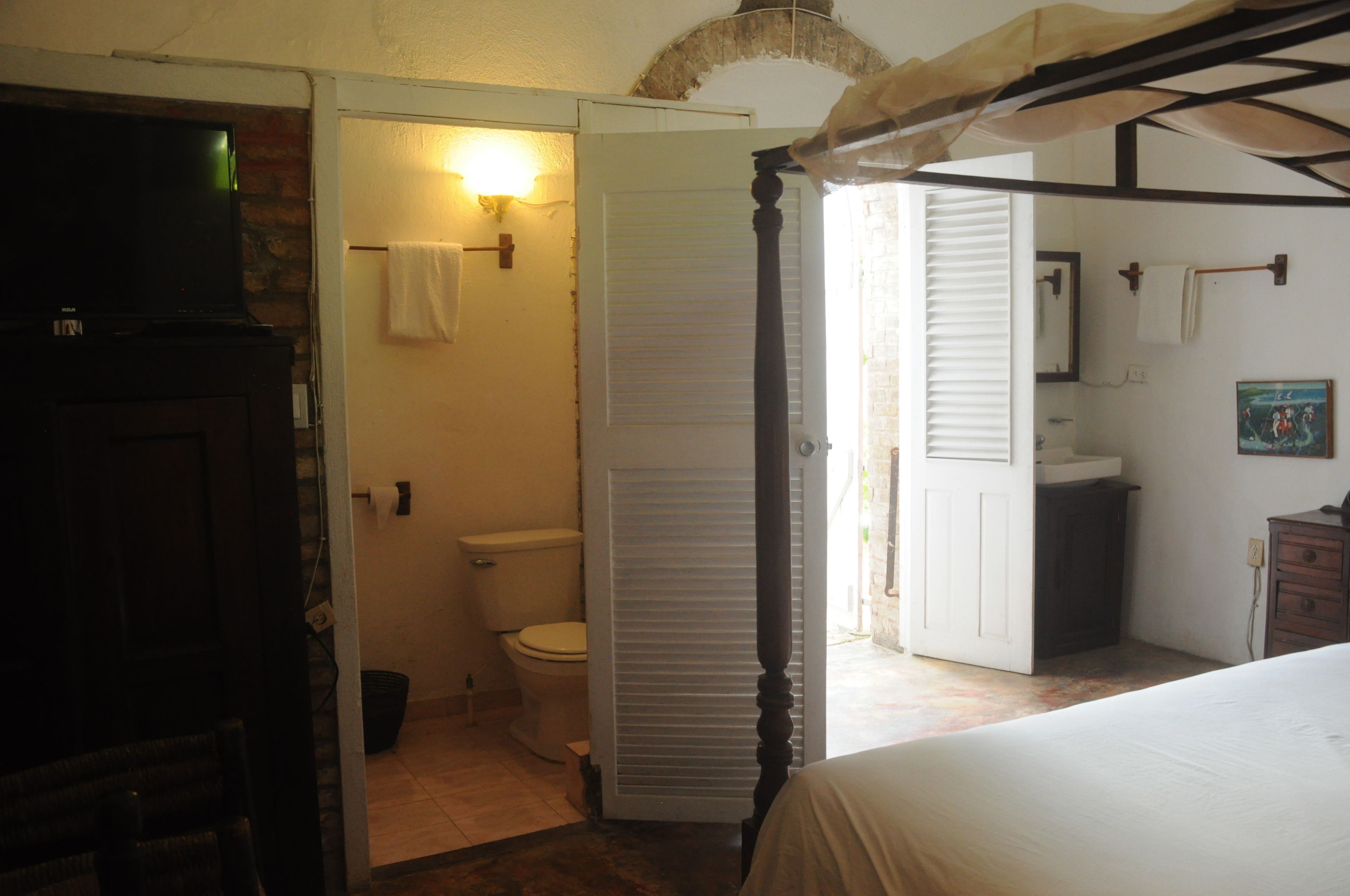 Une chambre à coucher avec un lit à baldaquin, une salle de bain avec des toilettes et un lavabo, et un téléviseur dans un coin.