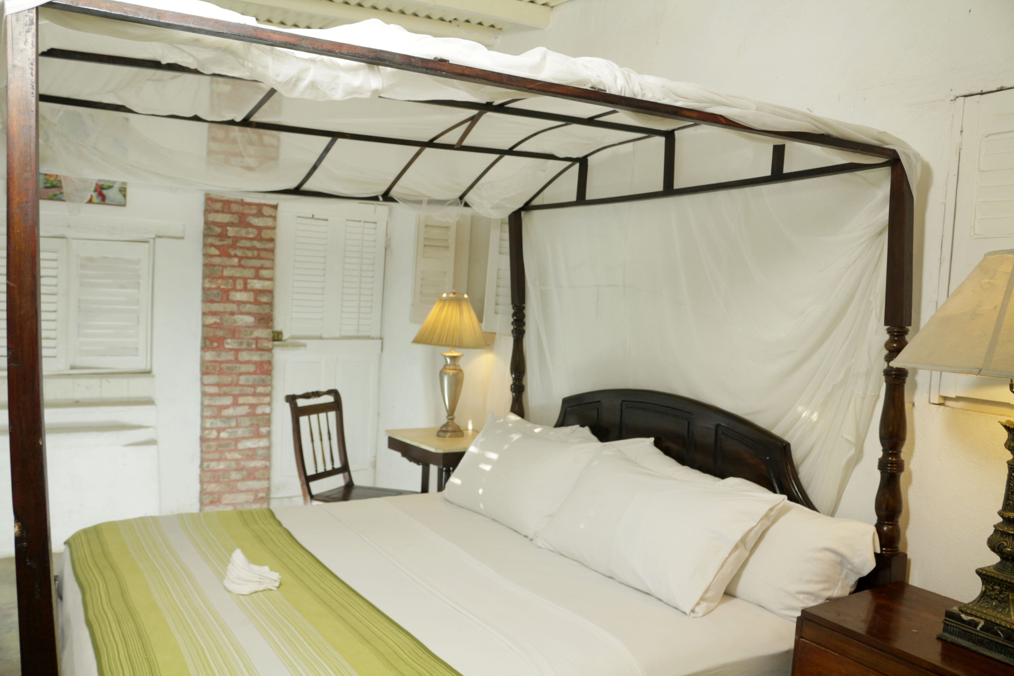 Ein Bett mit Himmelbett, ein Nachttisch mit Lampe, ein Sessel und eine Ziegelwand.