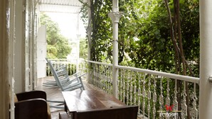 A covered outdoor seating area with a wooden table and chairs, surrounded by white railings and lush greenery.