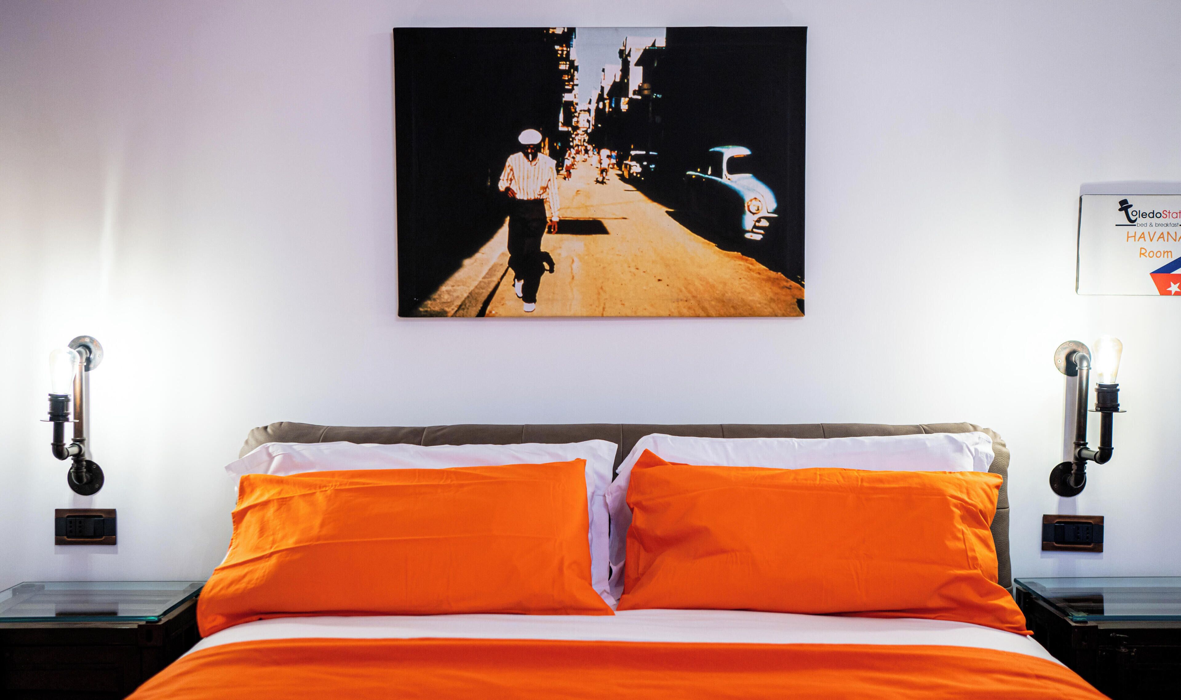 A hotel room with a bed, two nightstands, a wall-mounted painting, and a sign indicating a Havana Room.