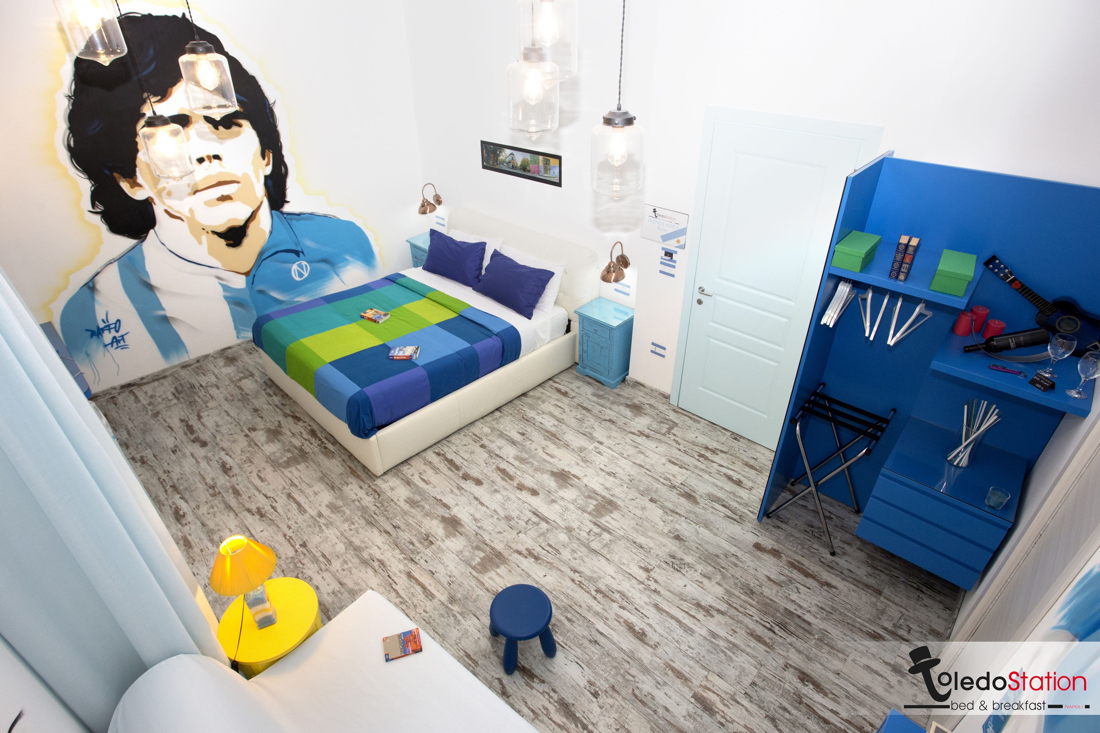 A bedroom with a bed, a nightstand, a blue wardrobe, and a wall-mounted shelf with toiletries.