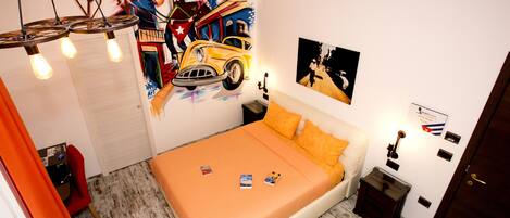 A bedroom with an orange bedspread, a mural on the wall, and a desk with a chair.