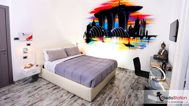 A bedroom with a bed, bedside table, and a wall mural of a cityscape. - Toledo station Bed & breakfast (Naples)