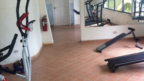 A gym with exercise equipment, a yellow exercise disc, and a door leading to another room. - Cap Lamandou Hotel (Jacmel)