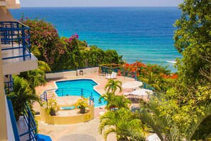 Zona de piscina con vista al océano, rodeada de follaje y palmeras.