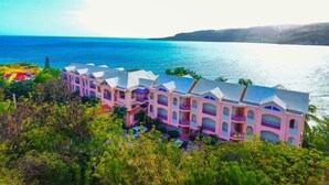 A row of pink buildings with balconies overlooking a body of water. - Cap Lamandou Hotel (Jacmel)