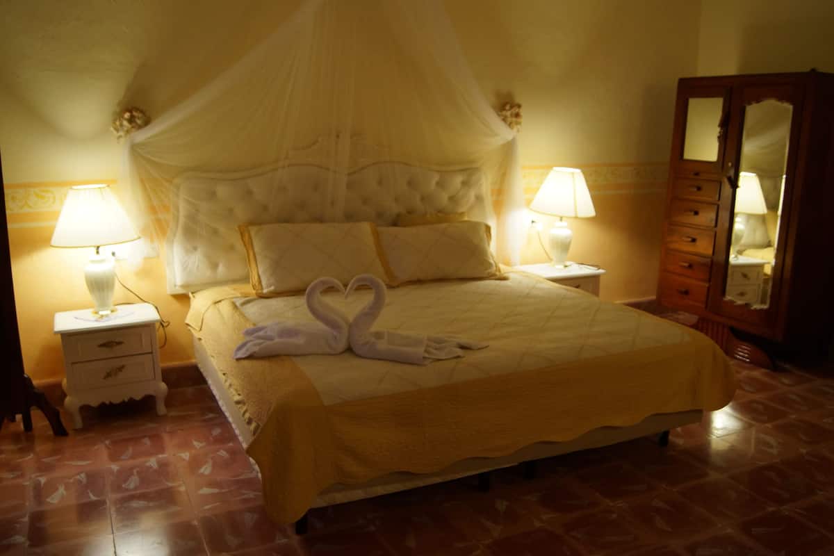 A hotel room with a bed, two bedside lamps, a nightstand, a mirror, and a decorative swan towel arrangement.
