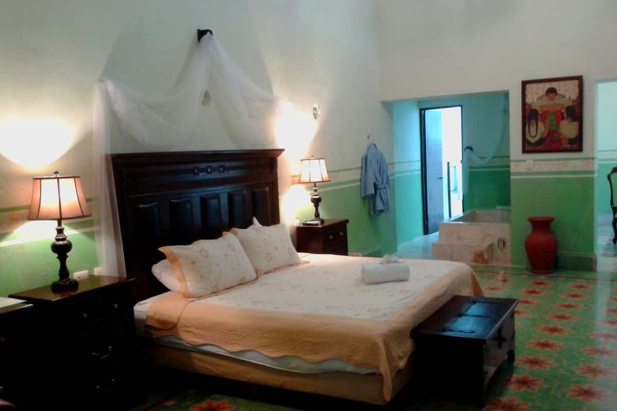 A hotel room with a bed, two bedside tables with lamps, a nightstand, a red vase, and a painting on the wall.
