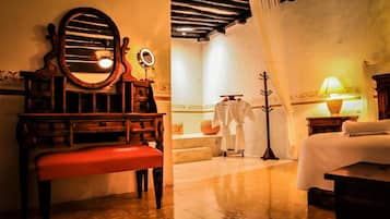 A room with a wooden vanity, a bench, a bed, a mirror, a lamp, and a coat rack.