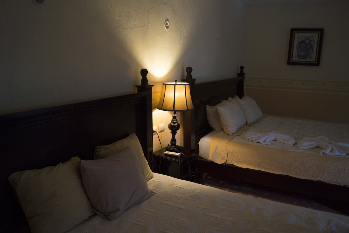 A hotel room with two beds, a nightstand with a lamp, and a framed picture on the wall.