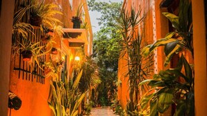 Un estrecho sendero de ladrillo flanqueado por edificios con plantas en macetas y una iluminación cálida.