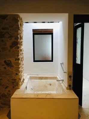 A modern bathroom with a freestanding bathtub, a small window, and a stone wall.