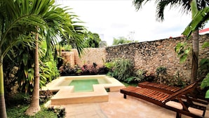 Un jardín con muro de piedra, una piscina pequeña y un banco de madera.
