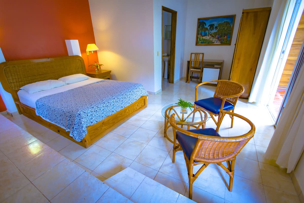 A hotel room with a bed, a small table with chairs, a lamp, and a painting on the wall.