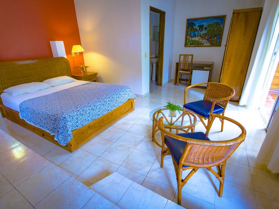 A hotel room with a bed, a small table with chairs, a lamp, and a painting on the wall.