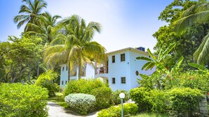 A white building with a balcony, surrounded by lush greenery and palm trees. - Hôtel Restaurant Cyvadier Plage (Jacmel)