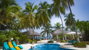 A pool area with lounge chairs, palm trees, and a view of the ocean. - Hôtel Restaurant Cyvadier Plage (Jacmel)