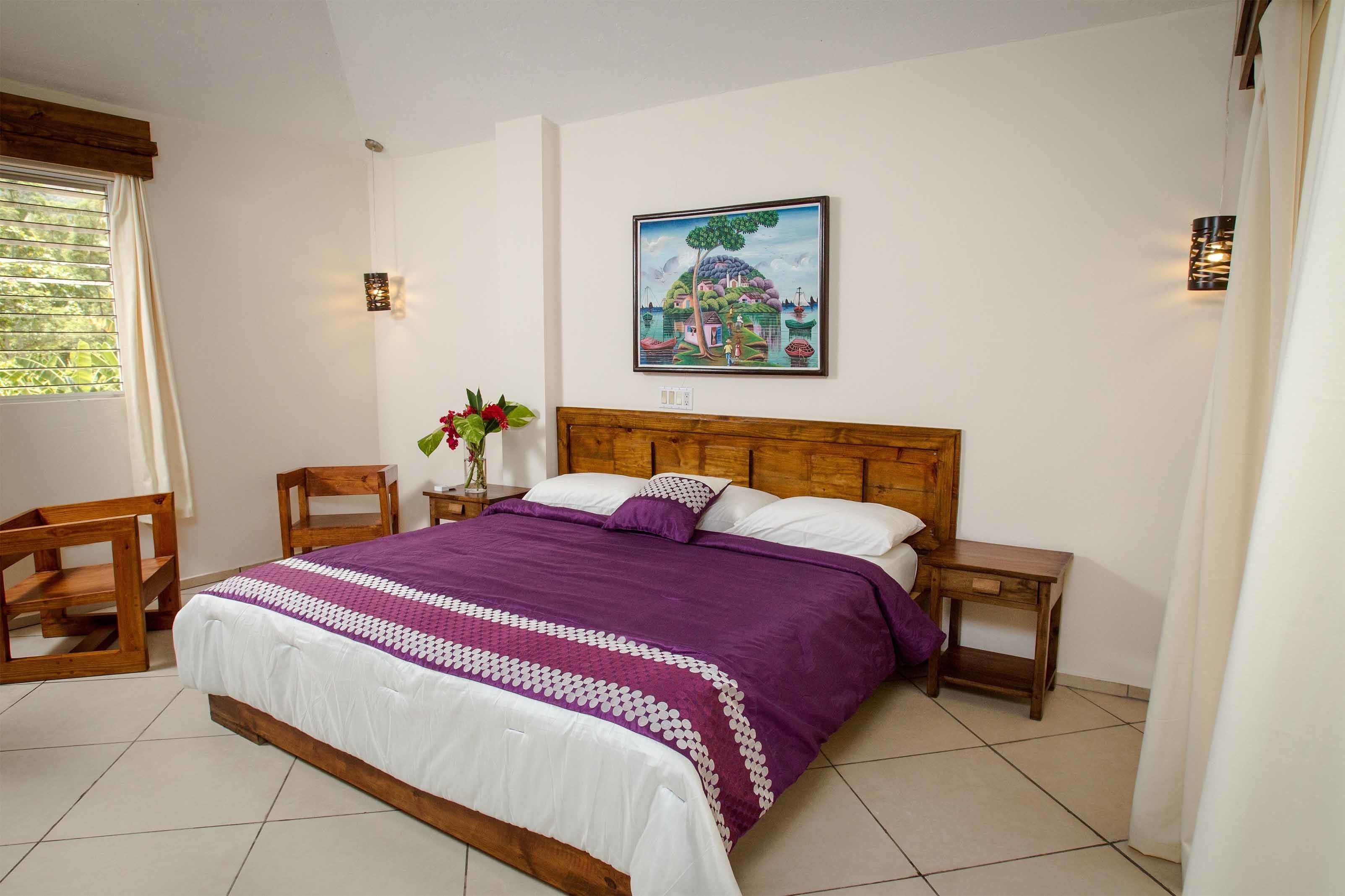 A bedroom with a wooden bed, a nightstand, a chair, and a painting on the wall.