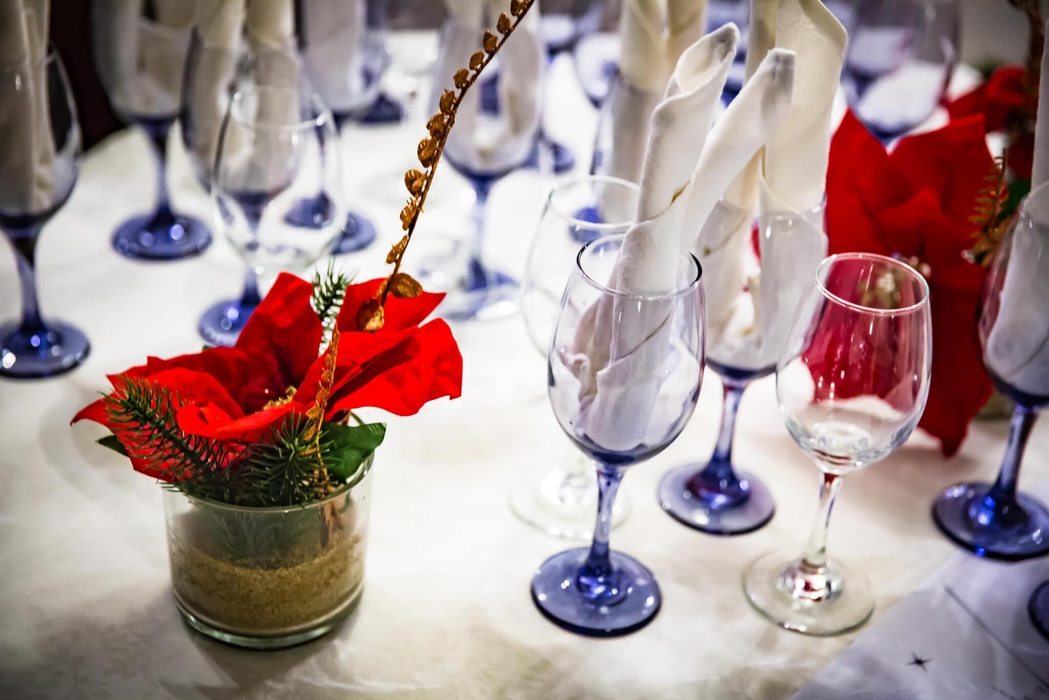 Une table mise avec un vase en verre contenant une composition florale rouge, des serviettes blanches et des verres à vin.