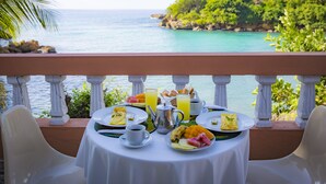 A table set for breakfast with a view of the ocean and a rocky island. - Hôtel Restaurant Cyvadier Plage (Jacmel)