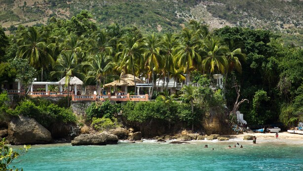 A coastal resort with palm trees, a beach, and a rocky cliff. - Hôtel Restaurant Cyvadier Plage (Jacmel)