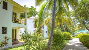 A two-story building with a balcony, surrounded by lush greenery and palm trees. - Hôtel Restaurant Cyvadier Plage (Jacmel)