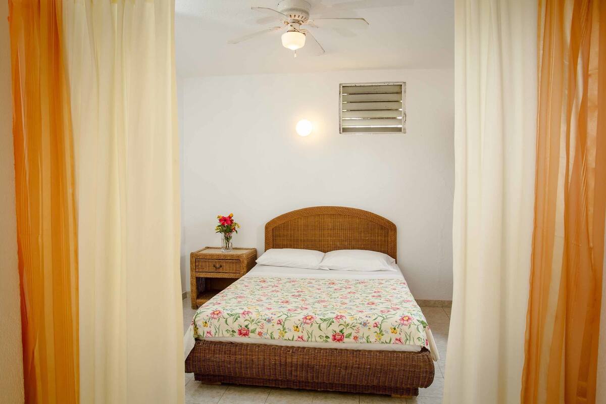 A bedroom with a bed, a nightstand, a wall-mounted light, and a ceiling fan.