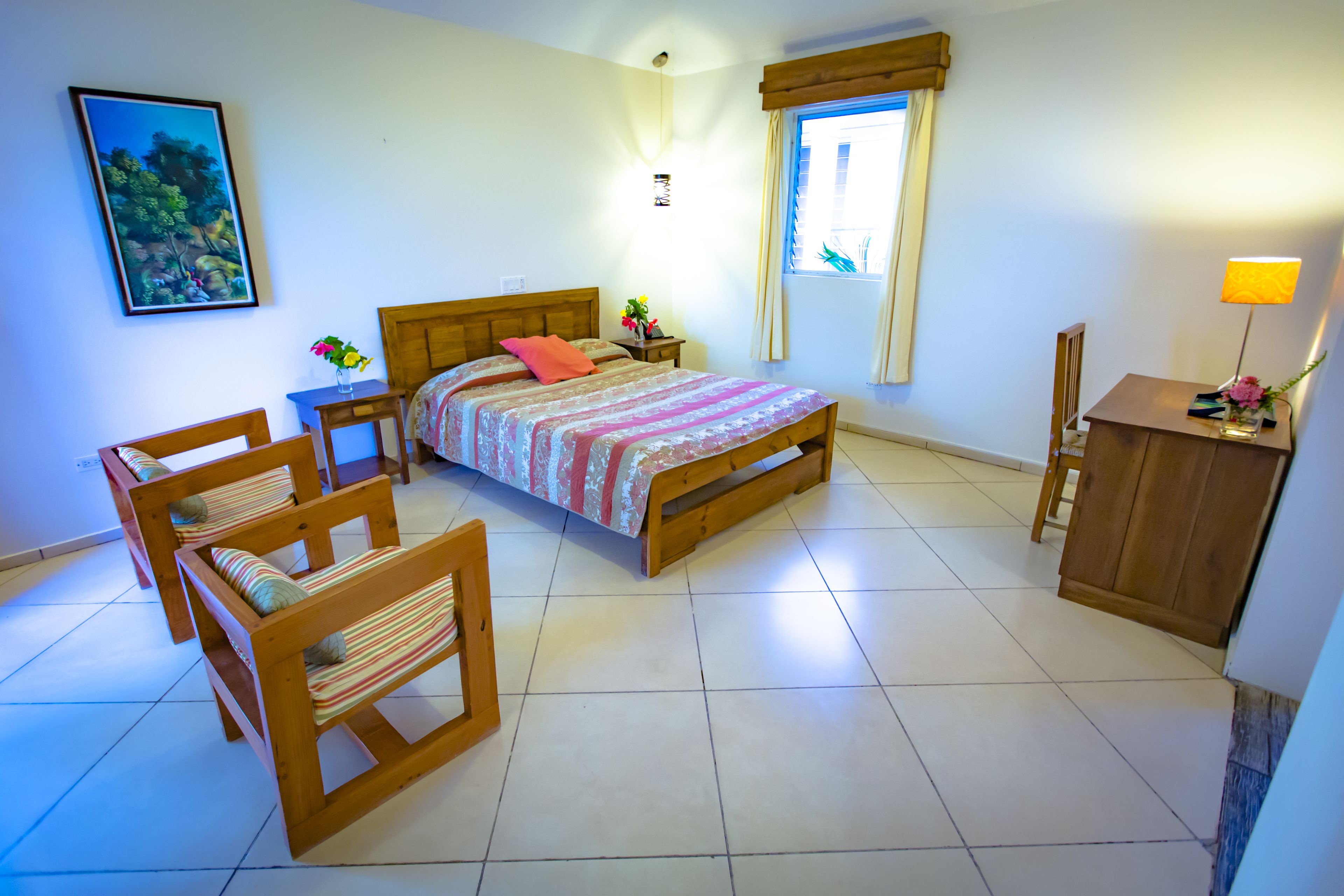 Un dormitorio con cama, dos sillas de madera, una mesita de noche, un escritorio y una ventana con cortinas.