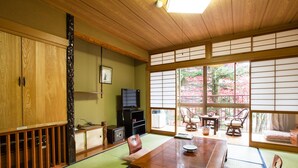 Une pièce de style japonais traditionnel, avec un sol recouvert de tatamis, une table en bois, des tapis de tatami, un téléviseur et une vue sur les cerisiers en fleurs.