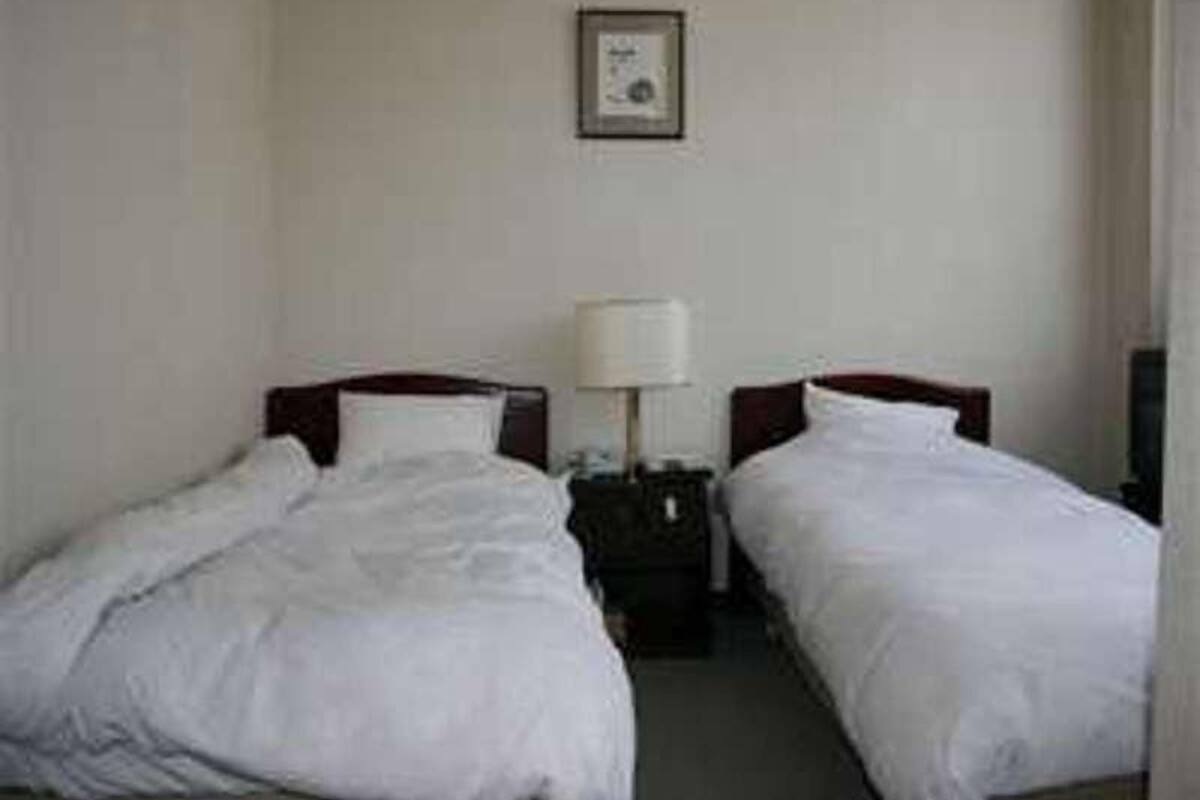 A hotel room with two single beds, a nightstand with a lamp, and a framed picture on the wall.
