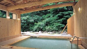 Un spa en bois doté d’une source d’eau chaude, entouré d’une végétation luxuriante.