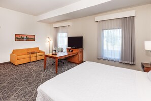 Une chambre d’hôtel avec un lit, un canapé, un bureau avec une télévision et un tableau représentant un paysage urbain.