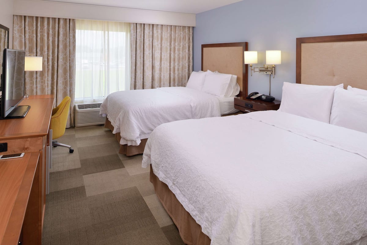 A hotel room with two beds, a desk, a chair, a TV, and a window with curtains.
