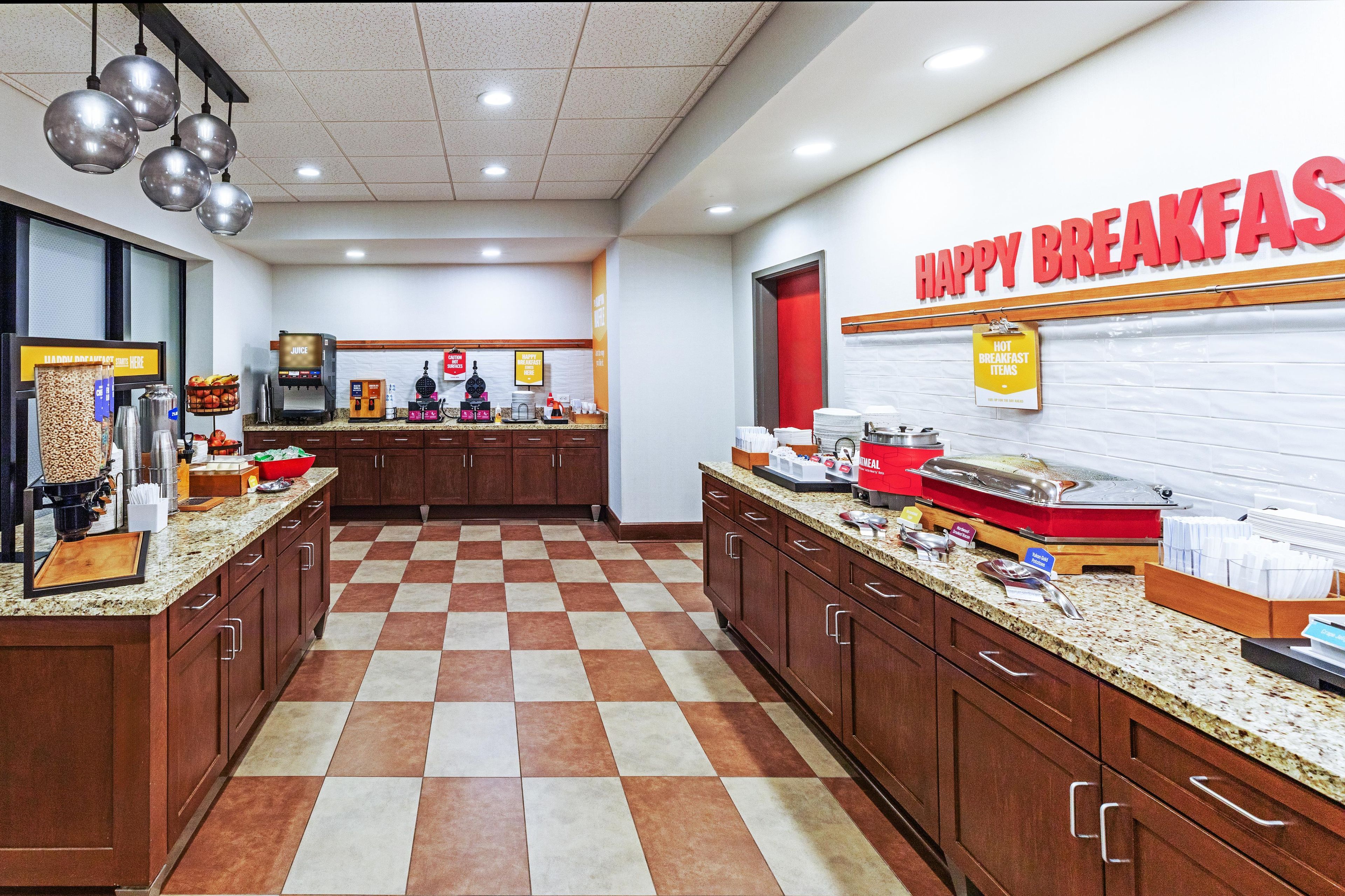 A breakfast area with a checkered floor, wooden cabinets, and a counter with various food items and a coffee machine.