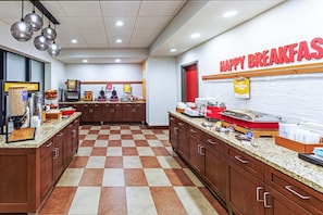 Un espace dédié au petit-déjeuner, avec un sol à carreaux, des meubles en bois et un comptoir où sont disposés divers aliments ainsi qu’une machine à café.