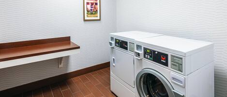 A laundry room with a white washing machine, wooden bench, and a framed picture on the wall.