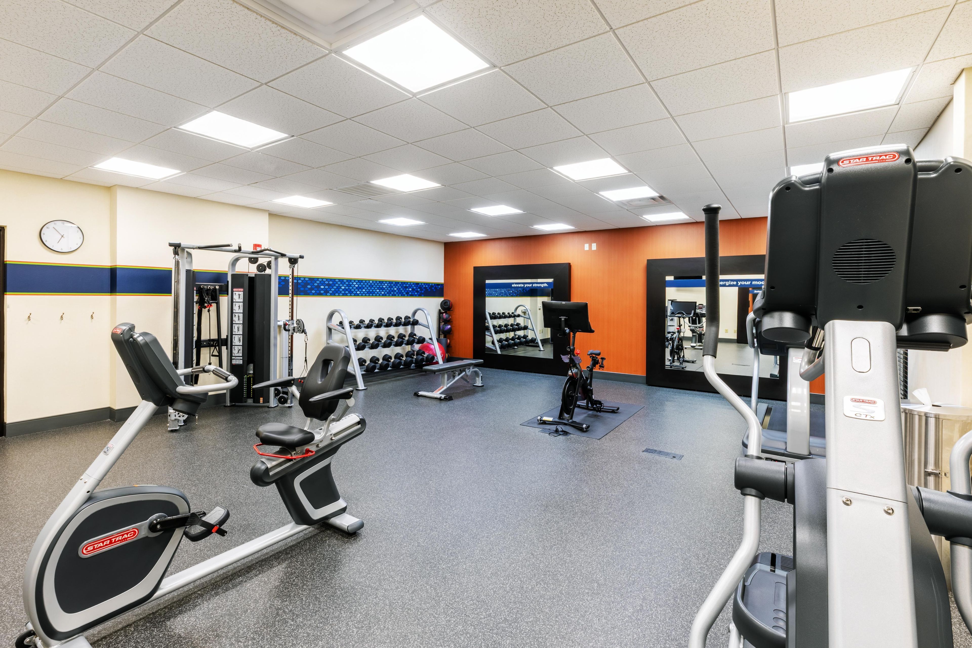 Une salle de sport équipée de divers appareils d’exercice, notamment des tapis de course, des appareils de musculation et des haltères.