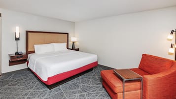 Une chambre d’hôtel avec un lit, des tables de chevet, une lampe, une chaise rouge et une petite table.