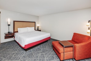 A hotel room with a bed, bedside tables, a lamp, a red chair, and a small table. - Hampton Inn & Suites by Hilton Lonoke (Lonoke)