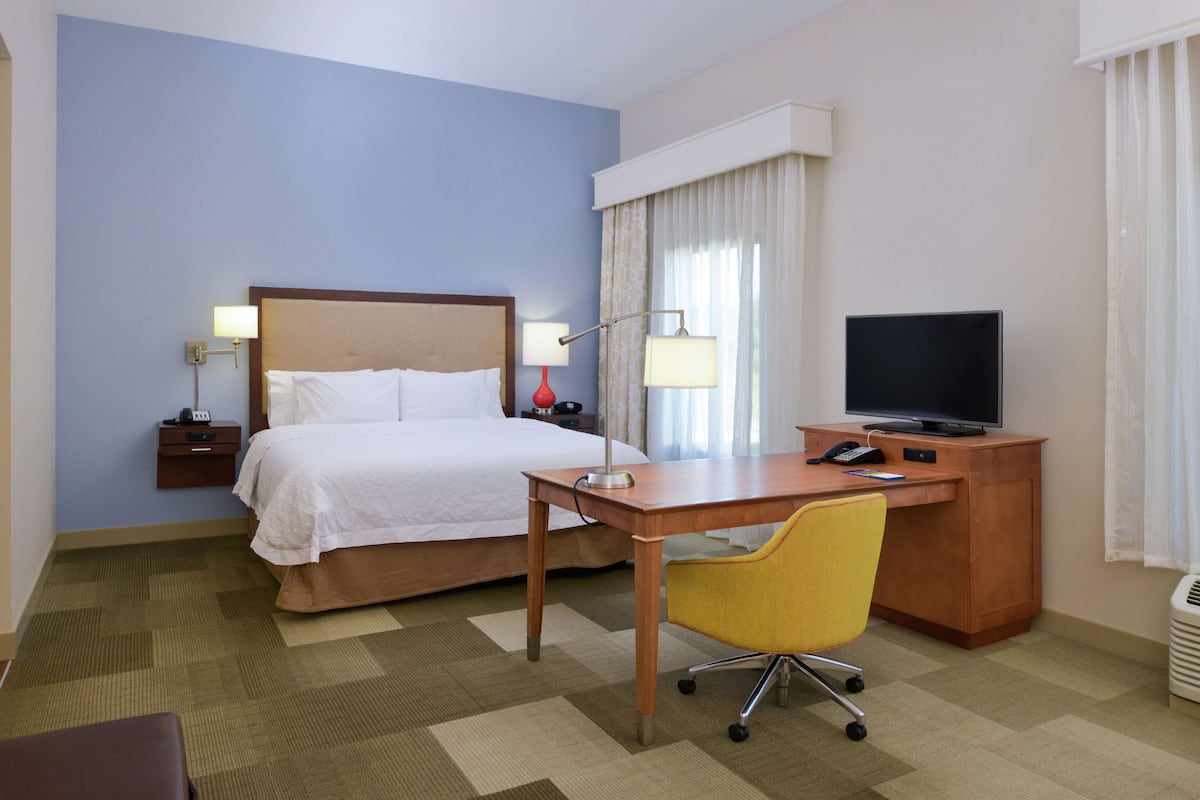 A hotel room with a bed, desk, chair, television, and lamps.