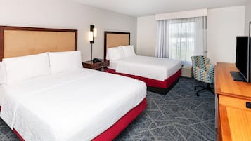 Habitación de hotel con dos camas, un escritorio, una silla, un televisor y una ventana con cortinas.