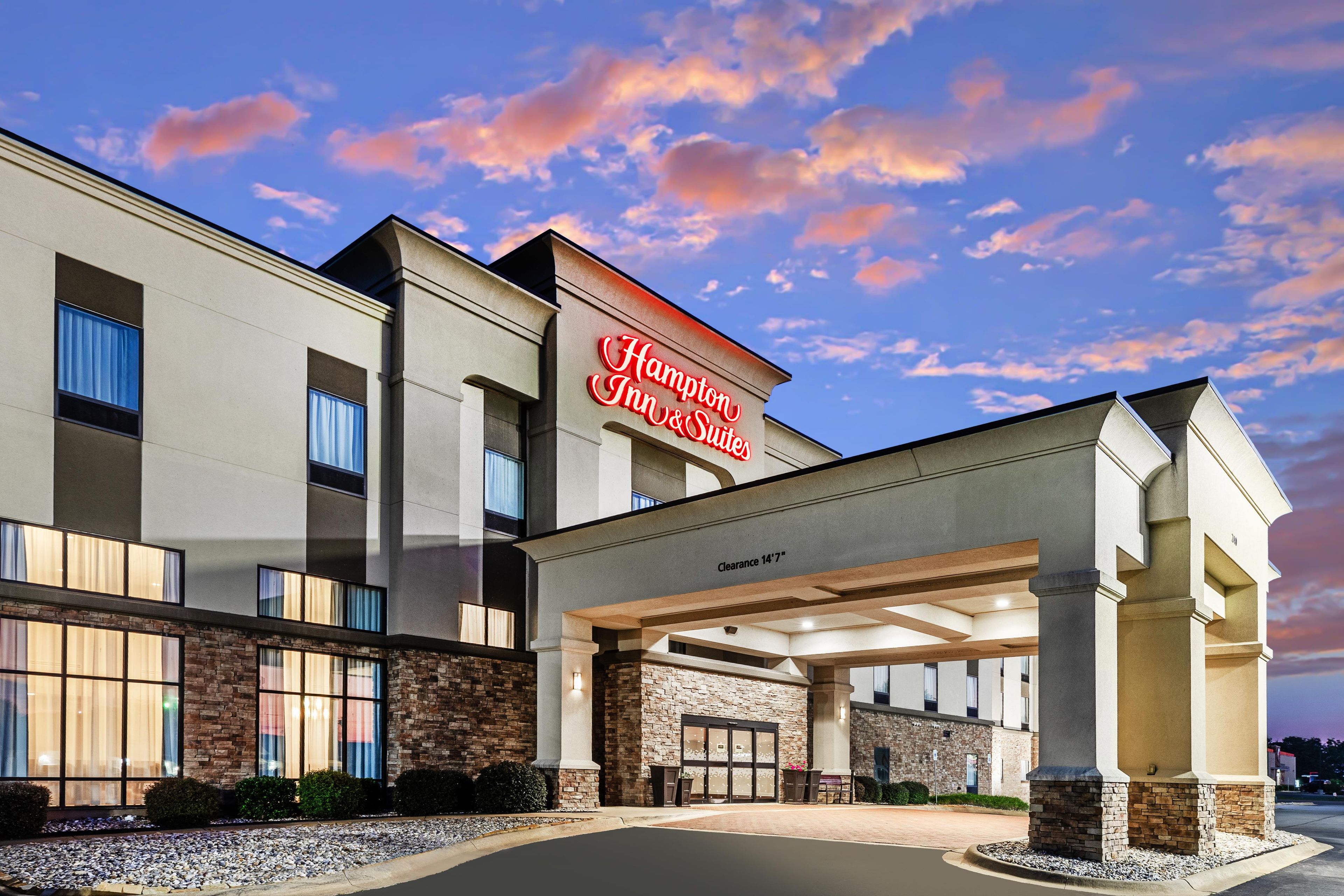 Un hôtel Hampton Inn & Suites doté d’une façade moderne, de grandes fenêtres et offrant une vue sur un ciel dégagé.