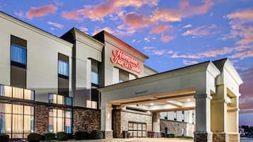 Un hôtel Hampton Inn & Suites doté d’une façade moderne, de grandes fenêtres et offrant une vue sur un ciel dégagé.
