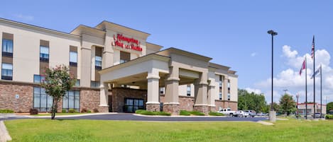 A Hampton Inn & Suites hotel with a modern facade, large windows, and a well-maintained lawn.