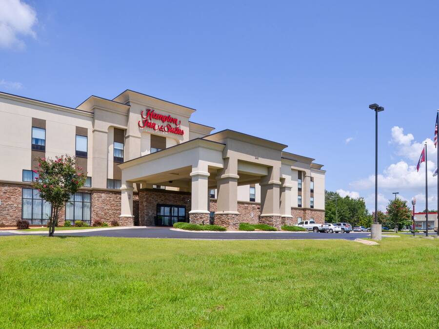 Um hotel Hampton Inn & Suites com fachada moderna, janelas amplas e gramado bem cuidado.