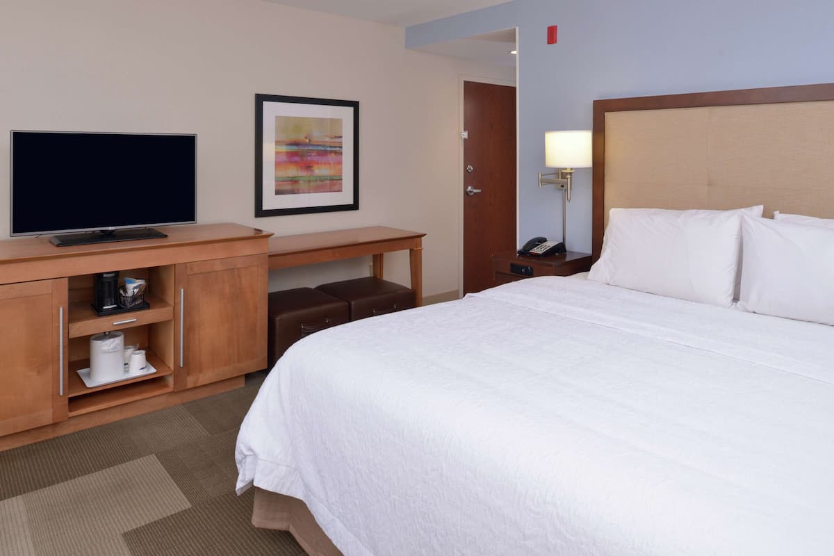 A hotel room with a bed, a TV on a wooden desk, a lamp, and a painting on the wall.