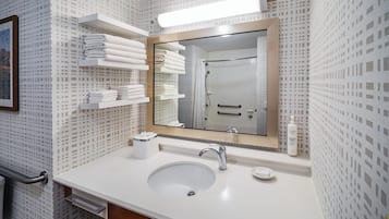 Un baño con lavamanos blanco, un espejo y repisas con toallas dobladas.