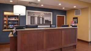 A reception desk with a counter, a large framed picture, a lamp, and a sign indicating Hilton Honors. - Hampton Inn & Suites by Hilton Lonoke (Lonoke)