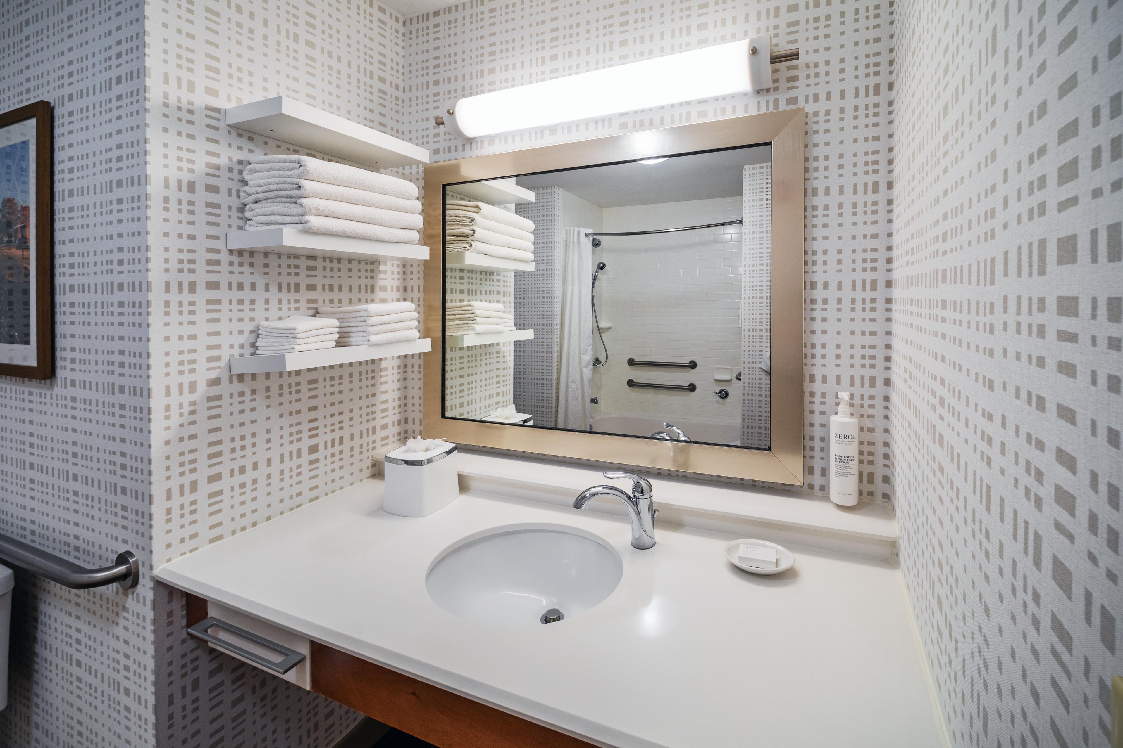 A bathroom with a white sink, a mirror, and shelves holding folded towels.