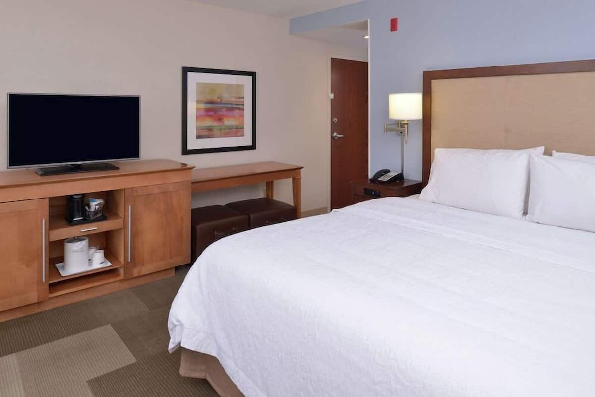 A hotel room with a bed, a TV, a desk with a lamp, and a painting on the wall.